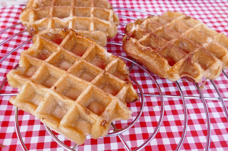 Three oval Liège waffles with a caramelized, crackly pearl-sugar crust, cooling on a rack