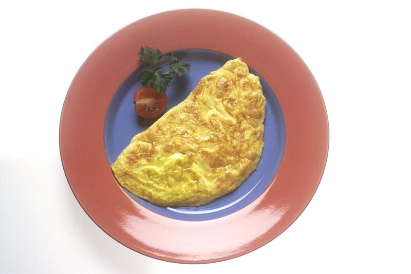Folded French omelette on a plate with a cherry tomato garnish